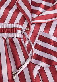 Röd och vit randig satinpyjamas med svarta accenter. Har en krage, en ficka och en smockad midja med knytning.