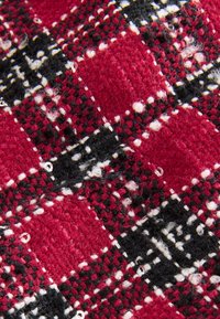 Rotes und schwarzes kariertes Stoffmuster mit weißen Akzenten, geprägt von einer strukturierten Webart und markanten quadratischen Mustern. Weiche, flauschige Oberfläche.