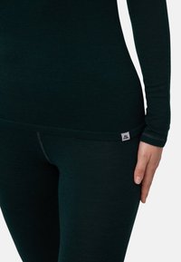 Haut thermique vert foncé et leggings en tissu doux et extensible. Présente une coupe ajustée et une petite étiquette de marque sur la ceinture.