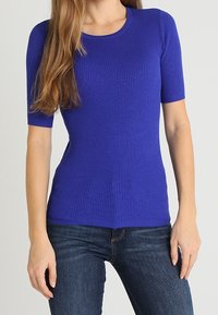 Ribbed, short-sleeved top in vibrant royal blue, featuring a round neckline and a fitted design, paired with dark blue jeans.
