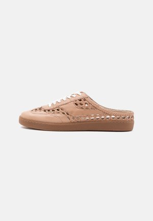 Μπεζ αθλητικό παπούτσι τύπου slip-on με λεπτομέρειες από πλεγμένο δέρμα, λευκά κορδόνια και επίπεδη καφέ λαστιχένια σόλα σε μονόχρωμο φόντο.
