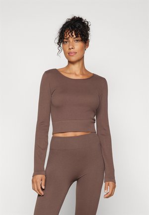 Brūns ribots garām piedurknēm crop tops, kas sader ar atbilstošām legingām. Abiem ir elastīga tekstūra un pieguļošs dizains ērtībai.