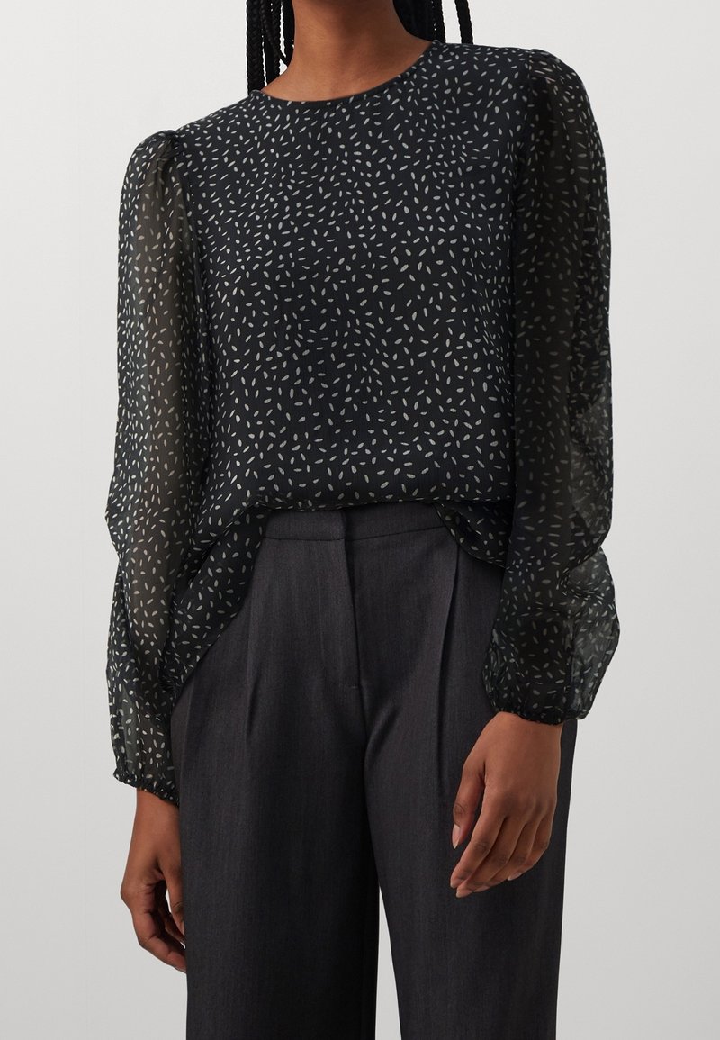 Svart blus med genomskinliga långa ärmar som har ett vitt lövmönster, rund halsringning och en lös passform, matchad med grå högmidjade byxor.