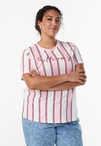 Light pink t-shirt with vertical maroon stripes and text "Belle en soi." Short sleeves, round neckline, paired with light blue patterned jeans.