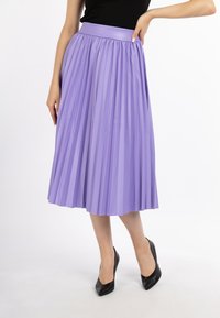 Plisseret lavendel midi nederdel med en glat, elastisk talje. Båret med sorte spidse hæle, der fremhæver et flydende design og blød tekstur.
