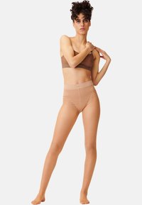 Shorts modellanti a vita alta in nude con una texture liscia, design senza cuciture e sottili accentuazioni a righe, abbinati a un top bandeau marrone.