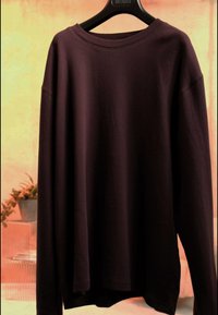 Chemise marron foncé à manches longues en maille gaufrée suspendue à un cintre en plastique noir sur un fond orange doux.