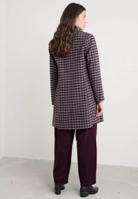 Karirana jakna u tamnozelenoj, burgundijskoj i krem boji; duži rukavi, do koljena, sa bočnim prorezima. Uparena s burgundijskim baršunastim hlačama i crnim cipelama.