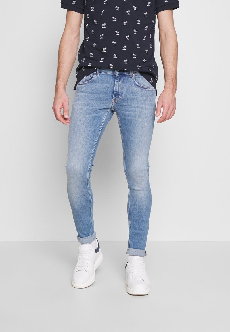 Ljusblå skinny jeans med en blekt textur och subtila sömnadsdetaljer, kombinerat med en svart t-shirt med kort ärm som har ett vitt palmträdsmönster.