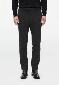 Pantaloni grigi a sigaretta realizzati in un tessuto testurizzato, con vita rilassata e una cintura, abbinati a mocassini in pelle nera.