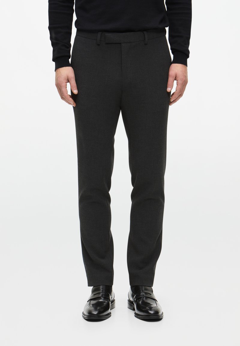 Pantaloni grigi a sigaretta realizzati in un tessuto testurizzato, con vita rilassata e una cintura, abbinati a mocassini in pelle nera.