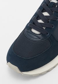 Sneaker blu navy realizzato in materiali scamosciati e in rete, con lacci, una tomaia testurizzata e una suola in gomma di colore chiaro.
