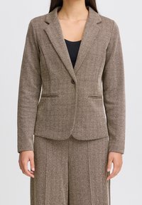 Blazer in tessuto micro rigato marrone con chiusura a un bottone, rever a picco e due tasche frontali. Vestibilità sartoriale e tessuto testurizzato.