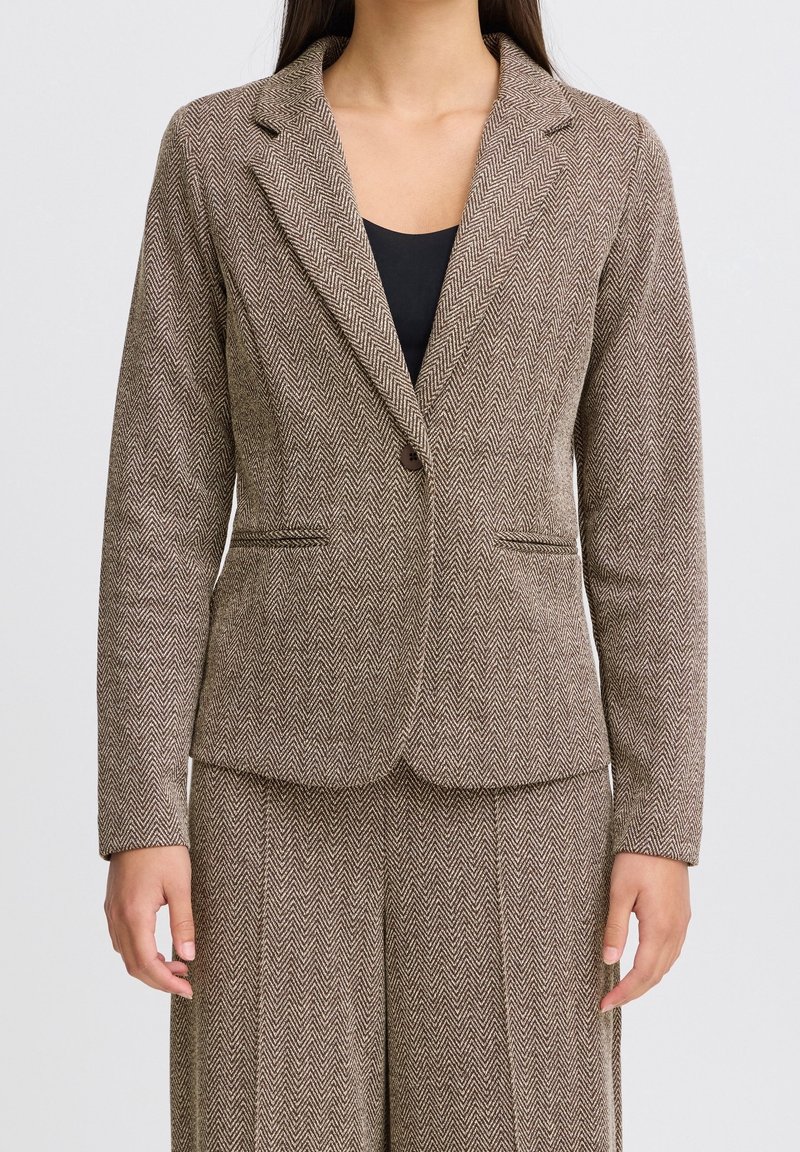 Blazer in tessuto micro rigato marrone con chiusura a un bottone, rever a picco e due tasche frontali. Vestibilità sartoriale e tessuto testurizzato.