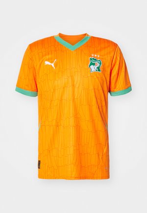 Oranž värvi jalgpallijersey tekstuurse mustriga, rohelised aktsendid krael ja varrukatel ning logo, mis sisaldab elevanti ja tähti.