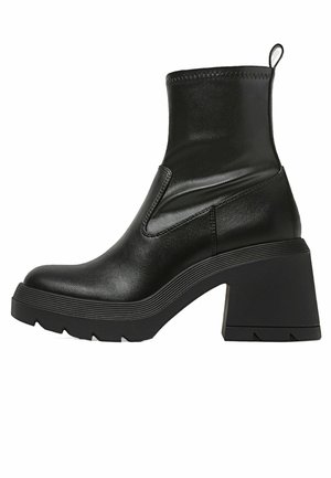 Stivaletto nero alla caviglia in pelle liscia con tacco spesso. Presenta pannelli laterali elastici e suola in gomma testurizzata.