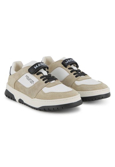 Baskets en daim beige et blanc avec des lacets noirs et des sangles portant l'inscription « MARC JACOBS » sur un fond blanc.