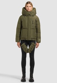 Veste matelassée vert olive avec un col montant, dotée de poches zippées, de coutures décoratives et d'accents matelassés amovibles à la taille.