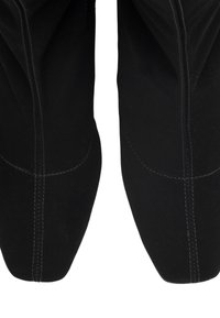Bottines en suede noir avec une texture lisse, un design à bout pointu et des coutures blanches contrastantes le long des coutures extérieures.