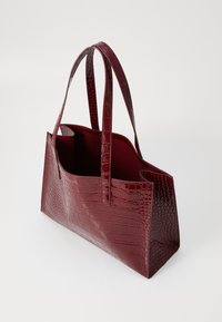 Sac fourre-tout texturé bordeaux en cuir verni, doté de poignées allongées et d'un haut ouvert, avec une forme rectangulaire structurée.