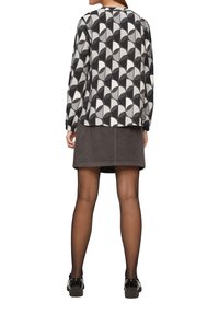 Chemise à manches longues avec un motif géométrique noir, blanc et gris, associée à une jupe en velours côtelé grise. Collants noirs et chaussures noires.