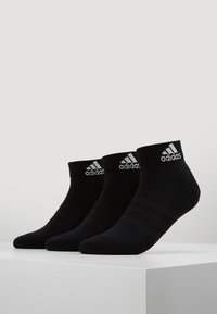 Tres pares de calcetines deportivos negros con puños acanalados y tres franjas horizontales. Presenta el logo de Adidas en blanco en el puño. Material de mezcla de algodón.