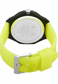 Reloj de acero inoxidable negro con caja redonda, correa de silicona amarilla, hebilla plateada y logotipo de la marca grabado en la parte posterior de la caja.
