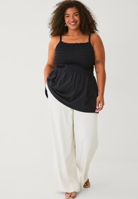 Zwarte gesmokt tanktop met verstelbare bandjes, gecombineerd met witte wijde broek. Soepele stof, relaxte pasvorm en geen zichtbare patronen.