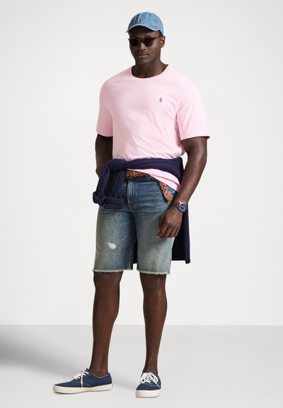 Rožinė trumpomis rankovėmis marškinėliai, mėlyna džinsinė kepurė, tamsiai mėlynas megztinis rišamas aplink juosmenį, nusidėvėję džinsiniai šortai, mėlyni sportbačiai. Kasdienis vasaros aprangos derinys.