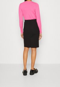 Zwarte kokerrok met een middellange snit, gecombineerd met een aansluitende roze trui met lange mouwen. Model draagt zwarte schoenen met gouden accenten.