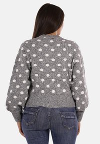 Maglione grigio lavorato a maglia con pois bianchi, orlo a coste e maniche a palloncino. Indossato con jeans blu, che mettono in evidenza il tessuto testurizzato e il motivo.