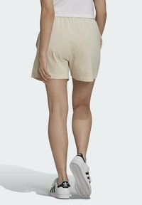 Beige bomullsshorts med elastisk midja, sidofickor och en avslappnad passform, kombinerat med vita sneakers med svarta detaljer.