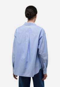 Chemise rayée bleu clair, manches longues, col boutonné, détail de pli au dos, coupe décontractée, en coton, et ourlet arrondi.