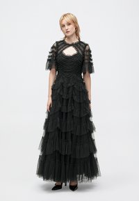 Czarna sukienka w warstwy wykonana z marszczonego tiulu, z krótkimi rękawami i dekoltem w kształcie łezki. Spódnica ma kilka warstw, co dodaje jej tekstury.