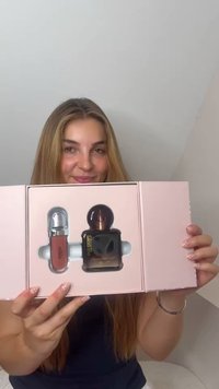 Jonge vrouw met lang haar houdt een open roze doos vast met Kiko lipgloss en een parfumflesje.