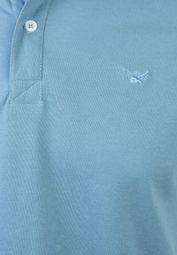 Camisa polo de color azul claro, hecha de tela texturada, con una tapeta de tres botones y un pequeño logo bordado en el lado izquierdo del pecho.