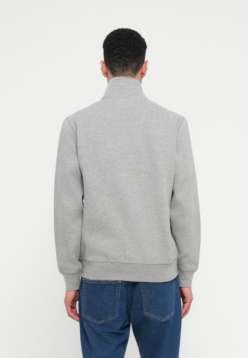 Sudadera gris con cuello alto, puños y dobladillo acanalados, hecha de una tela suave, combinada con jeans de mezclilla azules, vista desde la espalda.