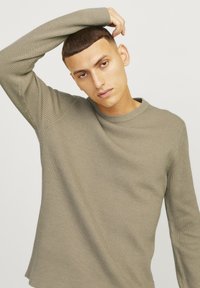 Pulover ribbed de culoare verde măsliniu deschis, cu mâneci lungi și guler rotund, având o finisare texturată și un stil ajustat.