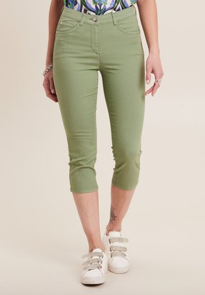 Pantaloni verdi cropped con un design aderente, realizzati in tessuto elasticizzato. Presentano cinque tasche e una chiusura con bottone frontale, abbinati a sneaker bianche.
