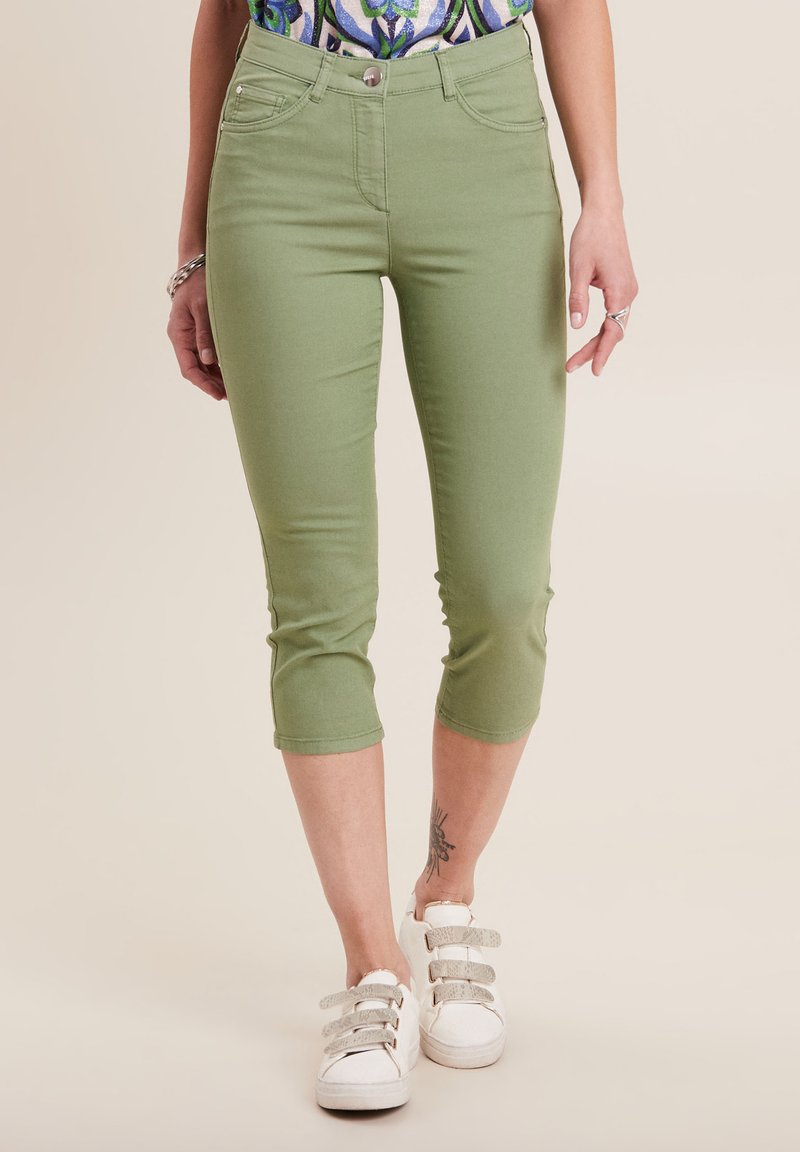 Pantaloni verdi cropped con un design aderente, realizzati in tessuto elasticizzato. Presentano cinque tasche e una chiusura con bottone frontale, abbinati a sneaker bianche.