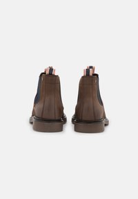 Botines de cuero marrón con paneles elásticos en navy, tiradores contrastantes en rayas rojas, blancas y azules, y una suela marrón resistente.