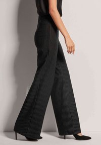 Zwarte, gestreepte broek met wijde pijpen gemaakt van een gladde stof; heeft een hoge taille en valt tot de vloer, gecombineerd met zwarte schoenen met een puntige neus.