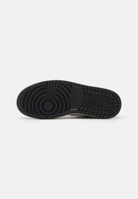 Semelle de chaussure Nike en caoutchouc noir avec des motifs de crampons circulaires et en grille, montrant le logo au centre sur un fond clair uni.