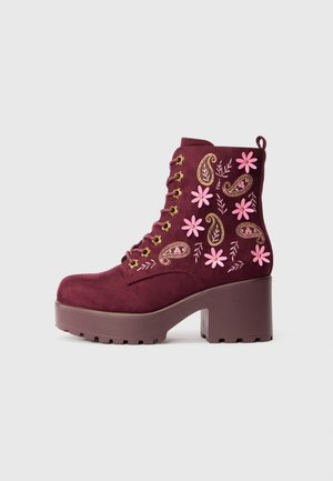Bottine en suède bordeaux avec broderies florales en rose et or, dotée d'un talon épais et d'un laçage avec œillets dorés.