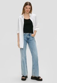 Biała, oversize koszula, czarny top na ramiączkach, jasnoniebieskie dżinsy typu wide-leg oraz czarne sandały na platformie. Gładki materiał, luźny krój, swobodny design.