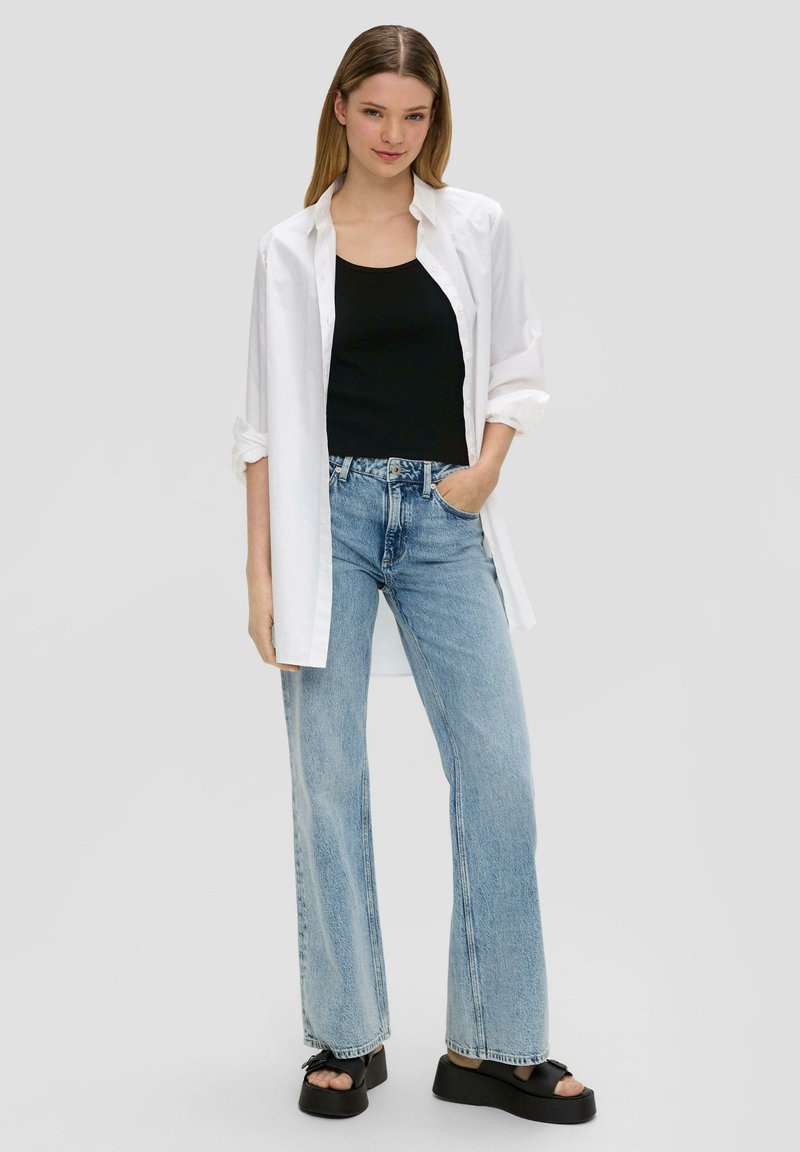 Biała, oversize koszula, czarny top na ramiączkach, jasnoniebieskie dżinsy typu wide-leg oraz czarne sandały na platformie. Gładki materiał, luźny krój, swobodny design.