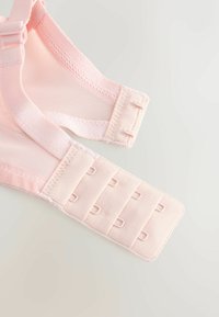 Bretelles de soutien-gorge roses douces avec fermetures ajustables à crochets et œillets, posées à plat sur une surface claire.