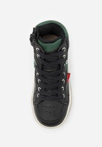 Zapatilla alta en cuero negro con detalles verdes, que presenta un cuello texturizado, suela blanca y cordones negros. Etiqueta de la marca roja visible.