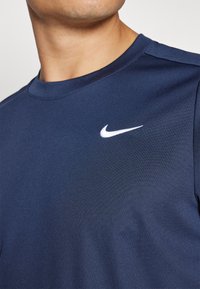 Camisola atlética azul-escura feita de tecido texturizado, apresentando um decote redondo e um logo branco da Nike na parte superior esquerda do peito.