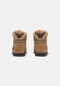 Braune Wildleder-Wanderschuhe mit gepolstertem Kragen, Gummisohlen und metallischen Logopunkten. Sie verfügen über ein robustes Design für Haltbarkeit und Unterstützung.